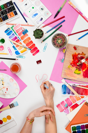 Flatlay with woman's hands, brush, paletts, pencils, watercolors, colored paper and other stationary supplies, artist or designer workplaceの写真素材