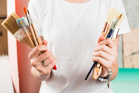 Closeup of woman's hands holding various paint brushes, selective shallow focusの写真素材