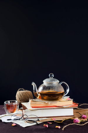 Glass kettle with black tea on vintage books with cup and glasses, selective focusの写真素材