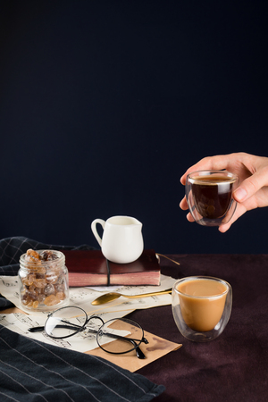 Closeup of two coffee, milk holder, jar with sugar, glasses and women hand holding cup with espresso, selective focusの写真素材