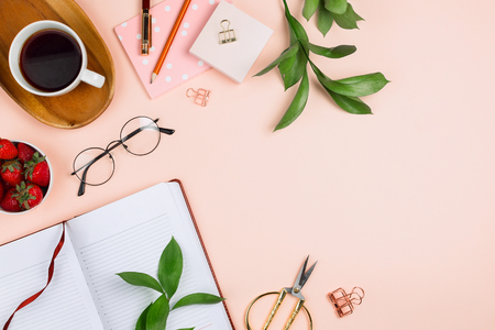 Business flatlay mockup with cup of coffee on a wooden tray, strawberries in a bowl, opened notebook, glasses, ruscus branches and other accessories on pastel background with copyspaceの写真素材