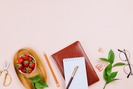Business flatlay mockup with strawberries on a wooden tray, notebooks, glasses, ruscus branches and other accessories on pastel background with copyspaceの写真素材