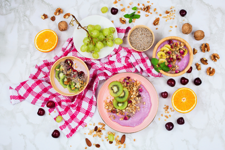 Flatlay with healthy vegan breakfast arrangement on marble background. Coconut and wooden bowls with smoothies, plant based yogurt, chia seeds and other ingredientsの写真素材