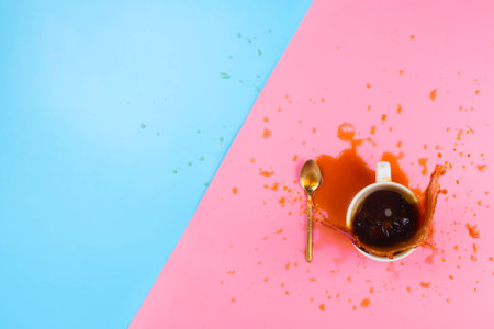 Flatlay with gold spoon and white mug with splashing coffee on pink and blue background with copyspaceの写真素材