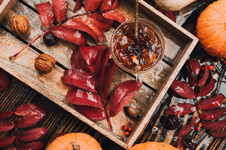 Autumn still life with glass tea cup and kettle in wooden tray with red leaves, pumpkins and squashes and falling raindropsの写真素材