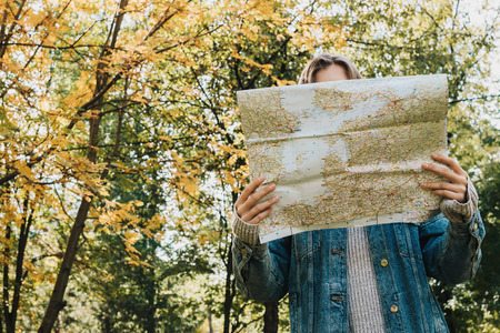 Lifestyle portrait from the back of young adult female in forest holding map in her hands, selective...