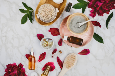 Flatlay of various beauty, bath and SPA products (serum, clay, essential oils, body brush, cream etc) and peony flower and petals on a marble backgroundの写真素材