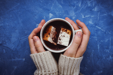 Flat lay of woman's hands in sweater holding cocoa or hot chocolate with homemade vegan marshmallowの写真素材