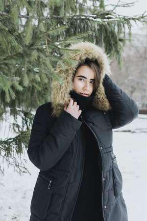 Lifestyle portrait of young adult female in warm winter clothing hiding in the hood, selective focusの写真素材