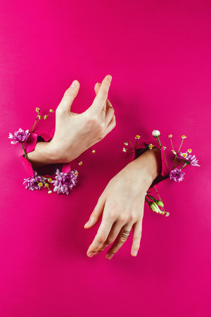 Closeup of woman's hands through torn paper filled with flowers, selective focusの写真素材