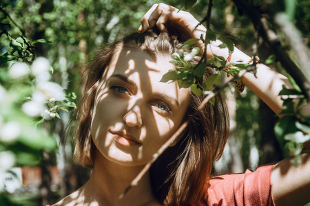 Spring or summer portrait of young adult white female in blooming spring trees, selective focus