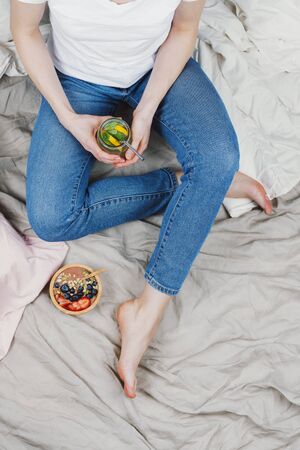 Above shot of woman sitting on a bed with healthy breakfast on sideの写真素材