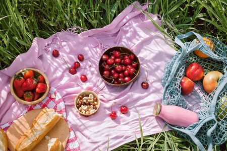 Zero waste summer picnic on the with cherries in the wooden coconut bowls, fresh bread and glass bottle of juice or smoothie on pink blanket, flatlayの写真素材