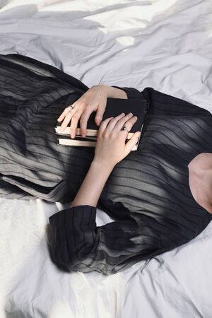 Faceless shot of woman lying in bed and holding pile of books, selective focusの写真素材