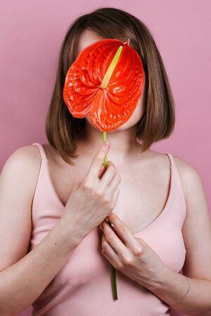 Portrait of woman's holding red peace lilly bloom (Spathiphyllum wallisii) in front of her face, selective focusの写真素材