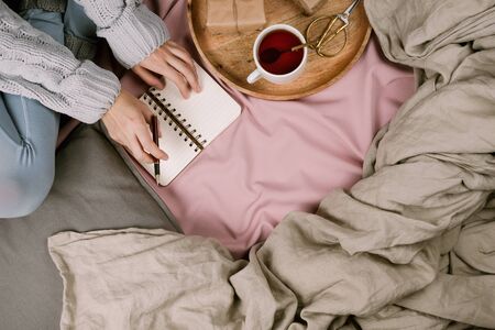 Cozy flatlay of woman's legs in blue leggins and warm grey socks in bed with cup of tea, selective focusの写真素材
