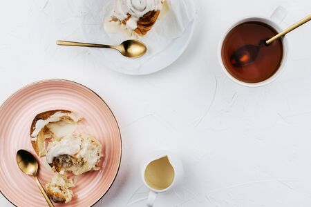 Flatlay of homemade cinnamon rolls with cream and tea on white cement backgroundの写真素材