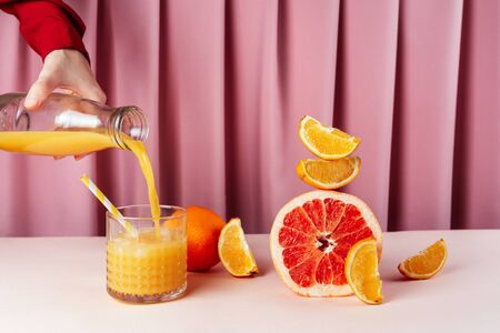 Woman pouring orange juice into the cup with ice on the table with various citrus fruits, selective focusの写真素材