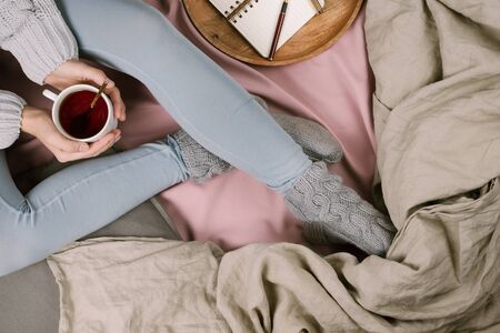 Cozy flatlay of woman's legs in blue leggins and warm grey socks in bed with cup of tea, selective focusの写真素材