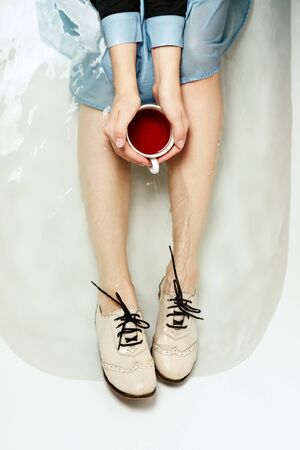 Top view of woman's legs in a bathtub with a cup of red tea, selective focusの写真素材