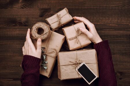 woman's hands in sweater holding wrapped presents and roll of string on wooden backgroundの写真素材