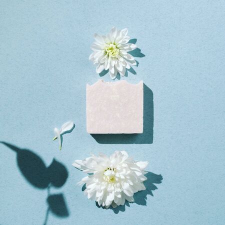 Minimalist flatlay of natural handmade soap with flowers and petals on blue backgound, square imageの写真素材