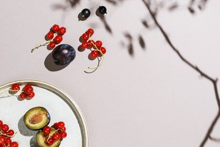 Minimalist flatlay of plums and berries on a handmade plate, selective focusの写真素材