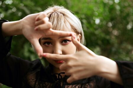 Closeup of young adult blond asian girl making frame gesture, selective focusの写真素材