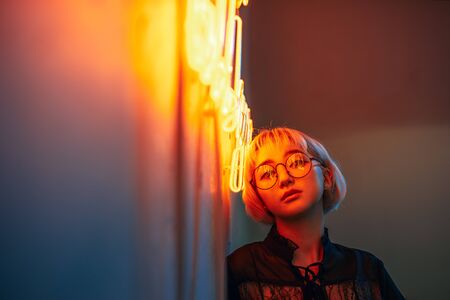 Young adult asian female wearing glasses in front of neon light sign, shallow selective focusの写真素材