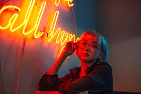 Young adult asian female wearing glasses in front of neon light sign, shallow selective focusの写真素材
