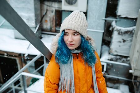 Young adult mixed asian female with blue hair standing outdoors during snowy winter weather, selective focusの写真素材