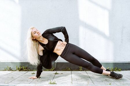 Young adult blond female doing side plank exercise outdoors, selective focus
