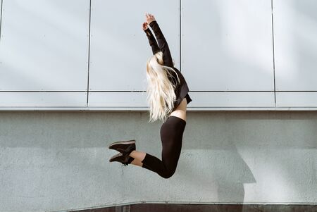 Young adult blond female athlete jumping in the air in front of grey wall, selective focusの写真素材