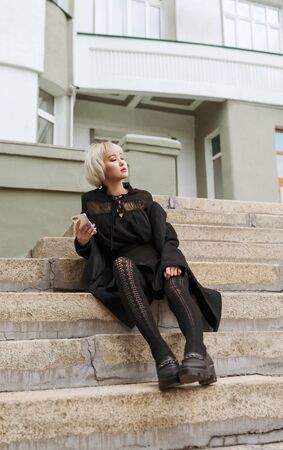 Young adult blond asian woman looking at her phone on stairs of building, selective focusの写真素材