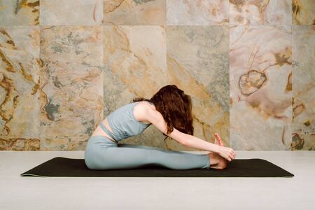 Young yoga practicing  variation pose in pastel blue leggingsの写真素材