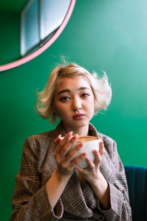 Young adult asian female drinking coffee in a coffeshop, selective focusの写真素材