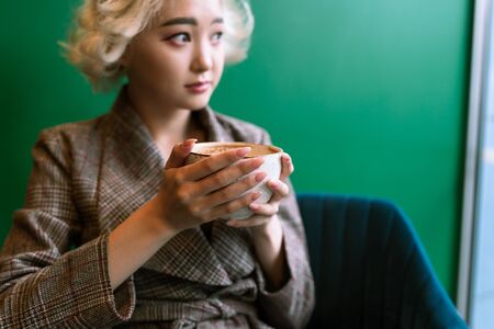 Young adult asian female drinking coffee in a coffeshop, selective focusの写真素材