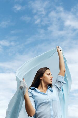 Young female holding cut of blue cloth up in the sky, selective focusの写真素材