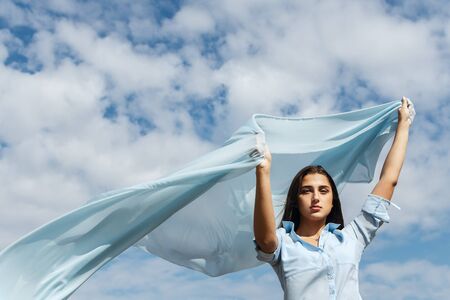 Young female holding cut of blue cloth up in the sky, selective focusの写真素材