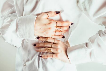 Closeup of white woman's hands with various rings around her waits, white shirt, white background, selective focus.の写真素材