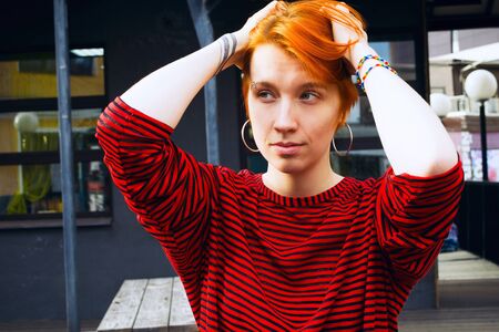 Young adult white woman in jeans jacket with died red hair touching her head, lifestyle portrait with selective focusの写真素材