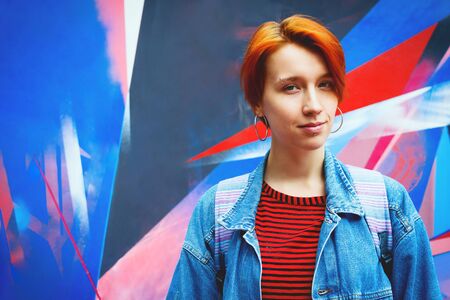 Young adult white woman in jeans jacket with died red hair, lifestyle portrait with selective focus