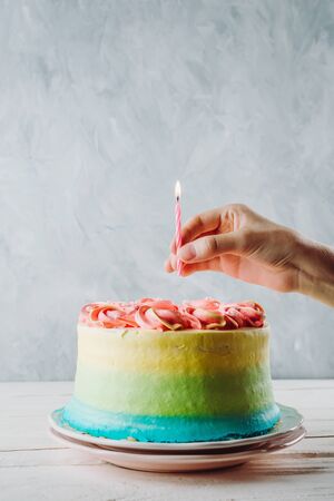 Closeup of colorful vegan cake and woman's hand holding birthday candle above it, selective focusの写真素材