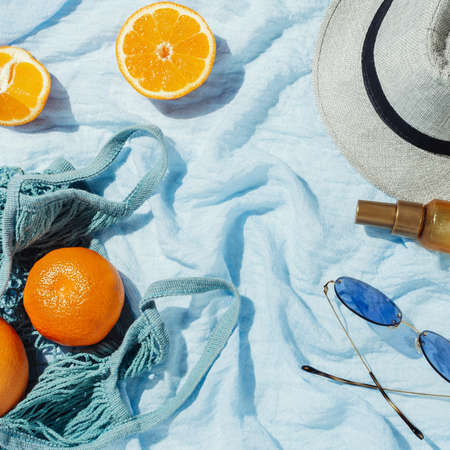Picnic flatlay of oranges in an eco string bag and hat on blue blanketの写真素材