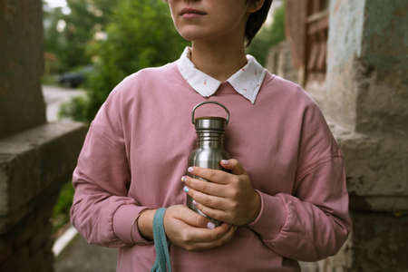Female in pink sweatshirt holding sustainable metal eco bottle in her hands outdoors