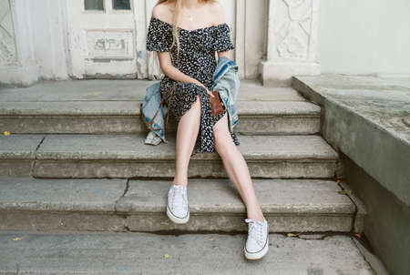 Faceless shot of young slim woman sitting on stairs outdoors holding camera in her handsの写真素材