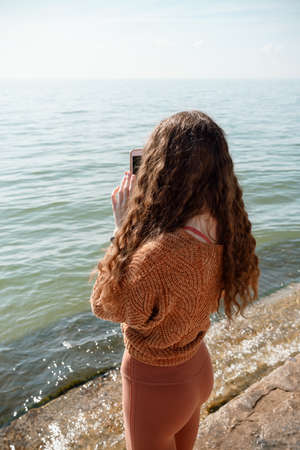 Female from the back filming video or making a picture on the beach using her smartphoneの写真素材