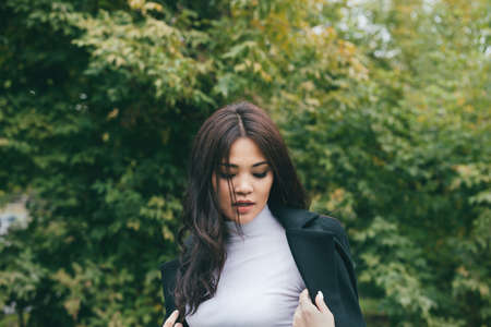 Beautiful portrait of young adult asian female in dark coat and white sweater outdoors