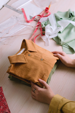 Closeup of female tailor folding orange shirt in small sewing workshopの写真素材
