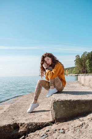 Woman in orange sweater sitting on a stone stairs on a beach with her eyes closed, selective focusの写真素材